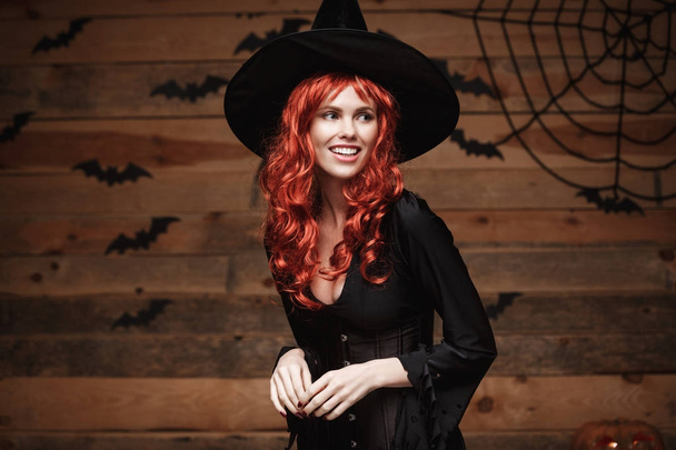 Koncepcja witch halloween - Happy Halloween czerwone włosy czarownica trzyma, pozowanie na stare drewniane studio tło. - Zdjęcie, obraz