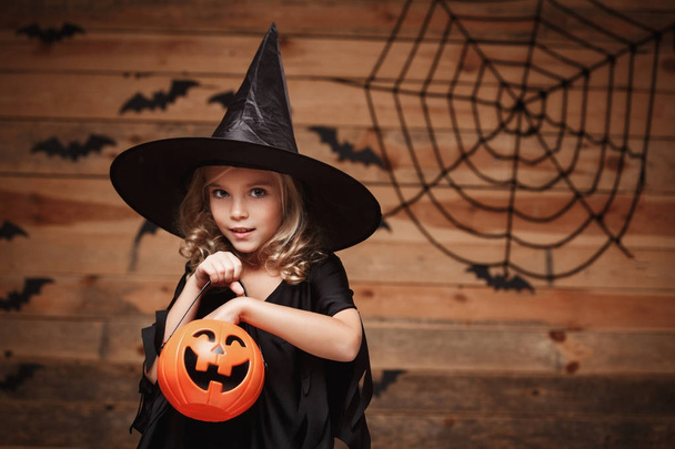 concepto de bruja de Halloween - pequeño niño bruja caucásica disfrutar con tarro de calabaza de caramelo de Halloween. sobre fondo de tela de murciélago y araña
. - Foto, Imagen