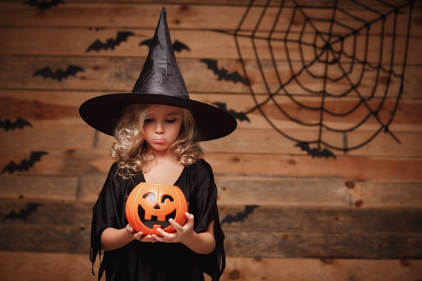 Concept de sorcière d'Halloween - petite sorcière caucasienne enfant décevante sans bonbons dans un pot de citrouille de bonbons d'Halloween. sur chauve-souris et toile d'araignée
. - Photo, image