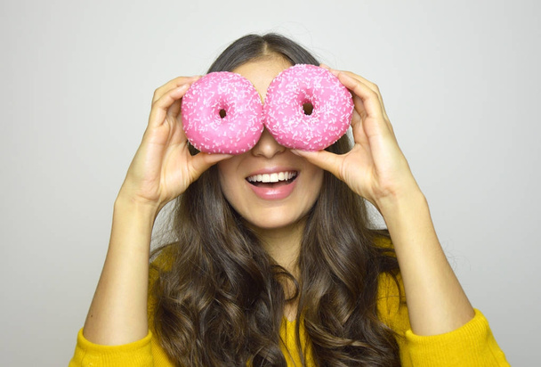 Portrait of smiling girl having fun with sweets isolated on gray background. Attractive young woman with long hair posing with doughnuts in her hands - Photo, image
