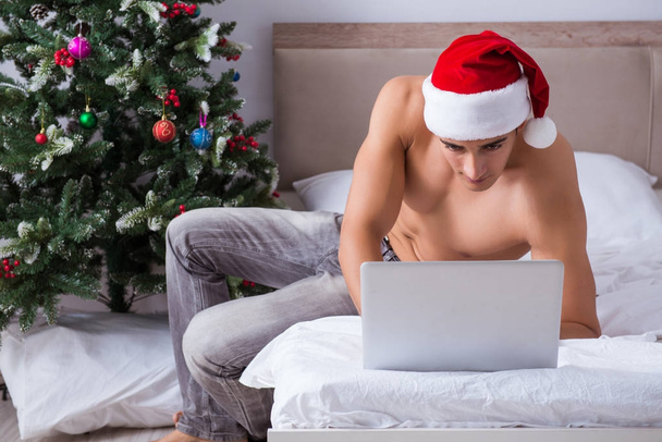 Seksikäs mies sängyssä yllään jouluhattu joulun konseptissa - Valokuva, kuva