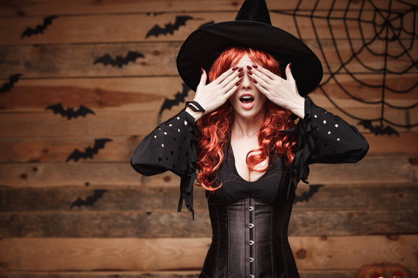 Concept de sorcière Halloween - Joyeux Halloween cheveux rouges Sorcière tenant les mains fermant les yeux posant sur un vieux fond de studio en bois
. - Photo, image