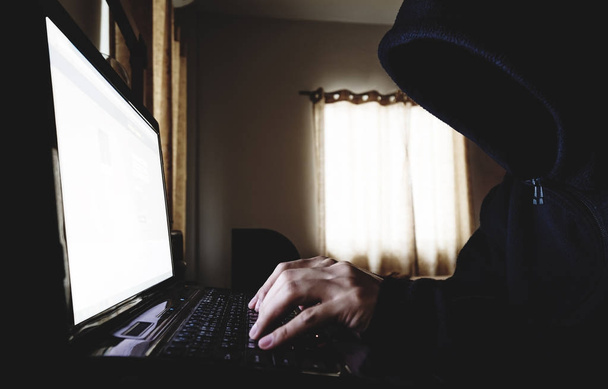 Αγνώστων στοιχείων χάκερ σε μαύρη κουκούλα χρησιμοποιώντας το φορητό υπολογιστή σε σκοτεινό δωμάτιο. Επιλεκτική εστίαση - Φωτογραφία, εικόνα