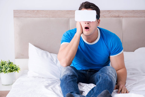 Junger Mann im Bett trägt Virtual-Reality-Kopfhörer - Foto, Bild