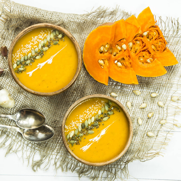 тыквенный суп в глиняном блюде, украшенном семенами тыквы, кунжутом, специями и сливками
 - Фото, изображение