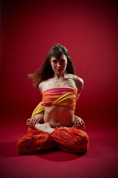 Beautiful sporty fit yogi woman practices yoga asana Padmasana - Lotus pose on the red background. studio shot - Foto, Imagem