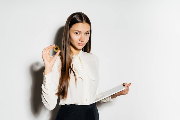 an office girl from a bank looking into the camera and holding some sort of paper and gold coin in her hand, isolated on a white background, crypto currency, bitcoins - Zdjęcie, obraz