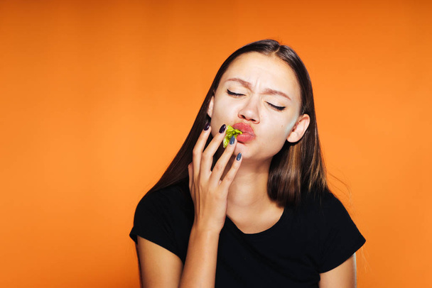 hungry girl eagerly finishes a hamburger, isolated on an orange background - Photo, Image