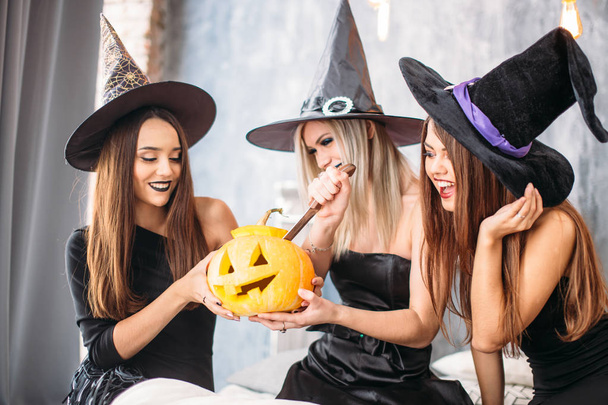 drei erwachsene Frauen schnitzen Halloween-Kürbisse, während sie lachen und feiern - Foto, Bild