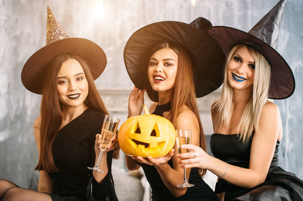 Halloween party. three girls drink champagne and sit on the bed - Фото, зображення