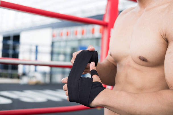 male fighter wear bandages on fist. muscular man bind bandage on - Photo, Image