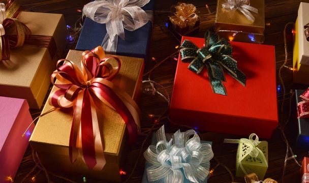 Mixture of gift boxes topped with ribbons decorated with festive lighting on wooden surface - 写真・画像