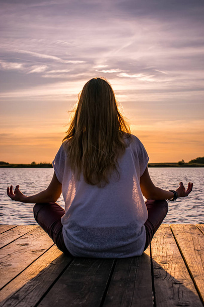 Göl kenarındaki ahşap duba üzerinde meditasyon yoga konumda genç kadın  - Fotoğraf, Görsel