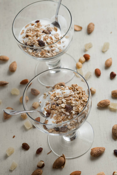Granola with yogurt, nuts and fruits in glass bowl on light background. Delicious, healthy sweet dessert for breakfast. Cereal, muesli. Copy space, closeup - Fotó, kép