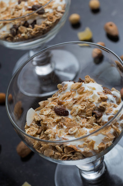 Muesli met yoghurt, noten en vruchten in glazen kom op donkere achtergrond. Heerlijke, gezonde zoete dessert voor het ontbijt. Granen, muesli. Kopie ruimte, close-up - Foto, afbeelding