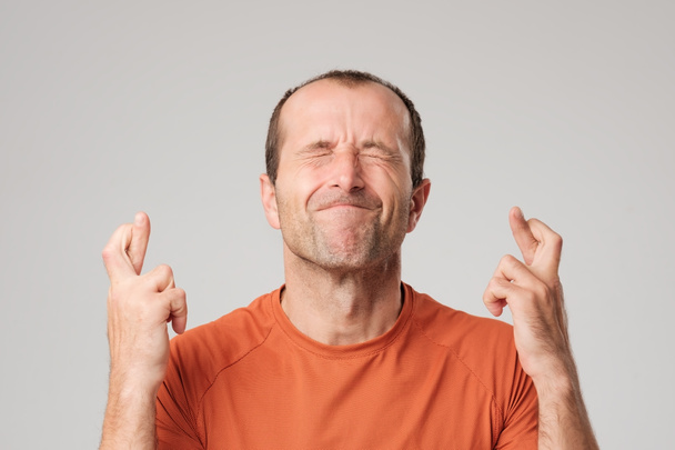 Зріла іспаномовний чоловік робить знак бажання з перехресними пальцями ізольовані на фоні
. - Фото, зображення