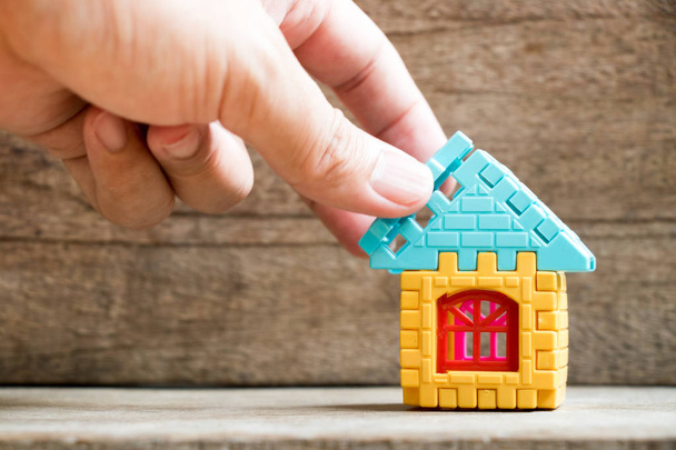 Mann hält Puzzleteil, um das Wohnmodellobjekt auf Holz-Hintergrund zu vervollständigen (Konzept des Traumhauses, Hypothekeninvestition, Erfüllung der Familie) - Foto, Bild