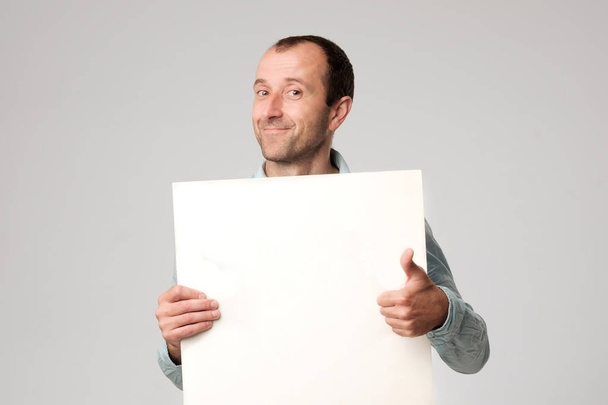 Ισπανόφωνος άνθρωπος κρατά το κενό σύμβολο σε ένα studio λευκό φόντο. - Φωτογραφία, εικόνα