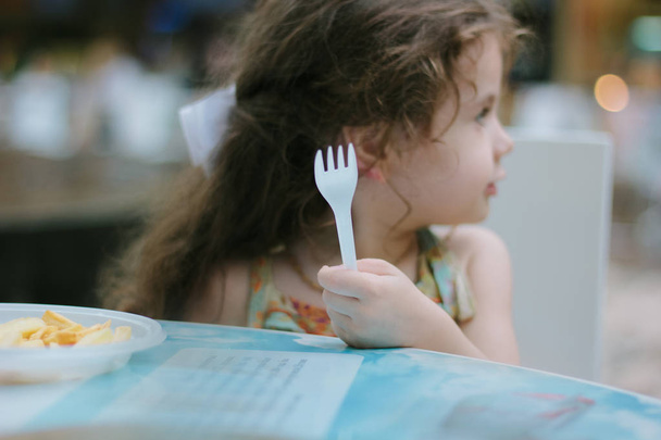 Mała dziewczynka z plastikowym widelcem w rękach w kawiarni lub restauracji - Zdjęcie, obraz