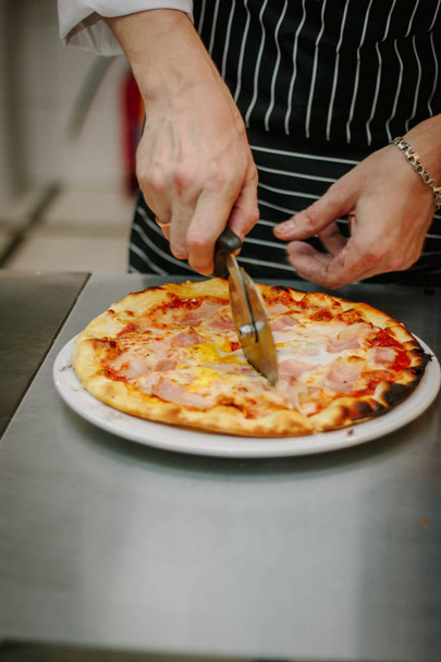 Chef coupant la pizza avec le coupe-pizza rond ou couteau
. - Photo, image