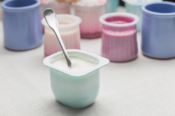 Yogurts assortment in plastic bowls on white textile background. Natural and fruit healthy, diet, gourmet dessert for granola breakfast. Sweet yogurts closeup - Foto, Bild