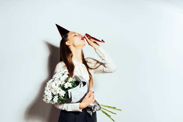 sweet girl blowing into the pipe. The girl is holding a bouquet of beautiful flowers. Happy birthday, holiday, fun - Foto, afbeelding