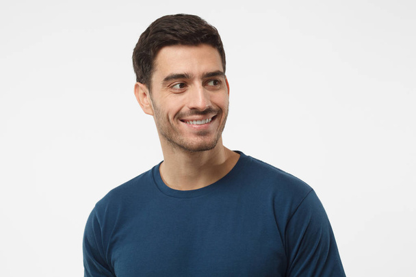 Close up portrait of smiling handsome male in blue t-shirt looking right, isolated on gray background - Photo, image