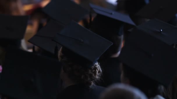 Mujeres jóvenes con vestidos académicos viendo la ceremonia de graduación en la universidad
 - Imágenes, Vídeo