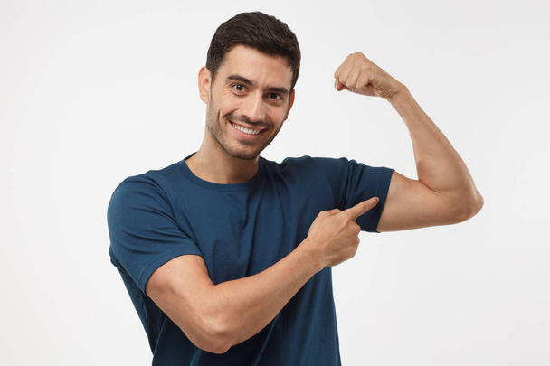 Young strong sporty man in blue t-shirt, shows biceps after training in gym, isolated on gray background - Foto, immagini