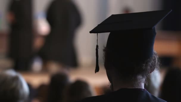 Curly hair man in mortarboard and academic dress looking at stage, graduation - Footage, Video