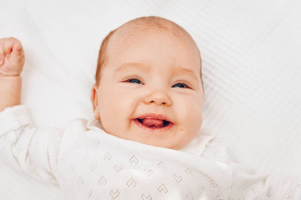 白い毛布の上に横たわると、笑みを浮かべて、心体を着ているかわいい赤ちゃん女の子 - 写真・画像