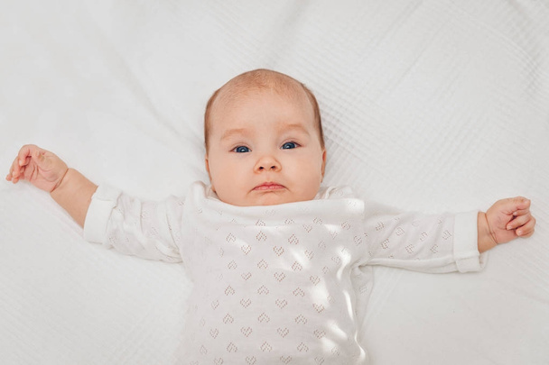 Αξιολάτρευτο μωρό κορίτσι ξαπλωμένο στο κουβέρτα λευκό και χαμογελαστός, φορώντας σώμα καρδιά - Φωτογραφία, εικόνα