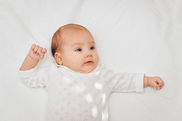 Schattig babymeisje liggend op witte deken en glimlachend, hart lichaam dragen - Foto, afbeelding