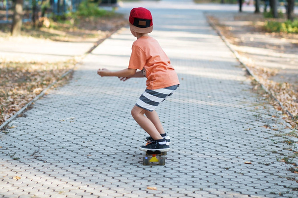 Little urban boy with a penny skateboard. Kid skating in a summe - Photo, Image