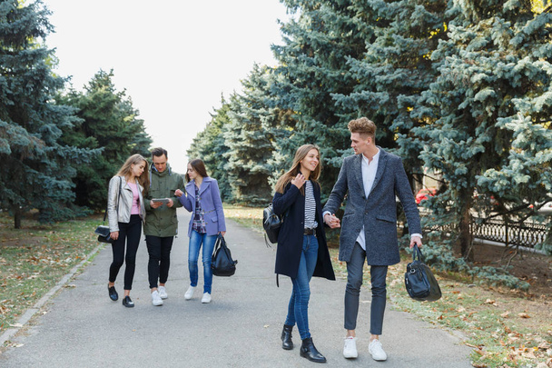 Young couple walking with friends. The guy holds the girls hand. - 写真・画像