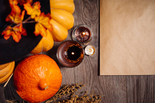 na dřevěné tabulce jsou oranžové a žluté dýně, svíčky jsou pálení a ležící podzimní listí zdobí dům pro halloween - Fotografie, Obrázek