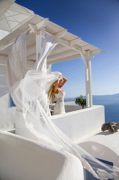 Όμορφη νύφη ξανθιά γυναίκα μοντέλο στο εκπληκτικό νυφικό θέτει στο νησί της Σαντορίνης στην Ελλάδα και πέρα είναι μια όμορφη θέα - Φωτογραφία, εικόνα