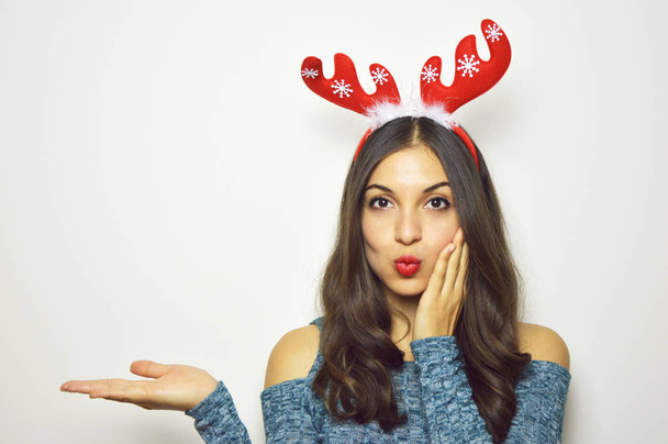 Beautiful young woman with reindeer horns on her head looks at camera and presenting your product on white background. Copy space. - Photo, Image
