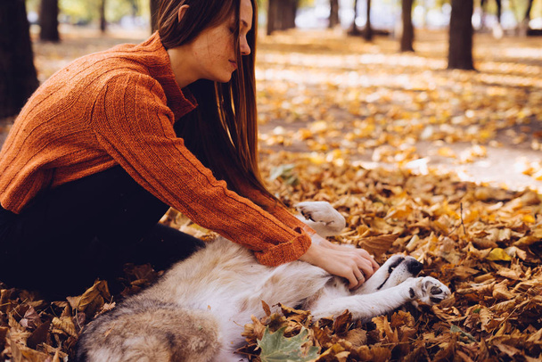 girl in a trendy orange sweater playing with her dog in the autumn park - Fotó, kép