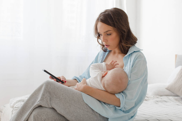 Woman using smartphone while breastfeeding - Fotoğraf, Görsel