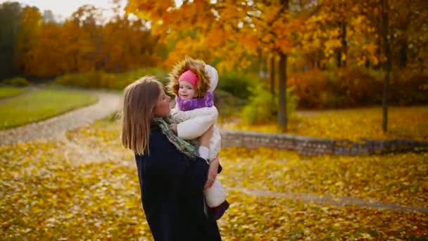 ősszel, amikor a sárga levelek körül anya és lány játszik a juhar leveleket, nevetett, és mosolygott. Anya ölelést és játszik az én lányom ősszel. Bokeh és napfény. - Felvétel, videó
