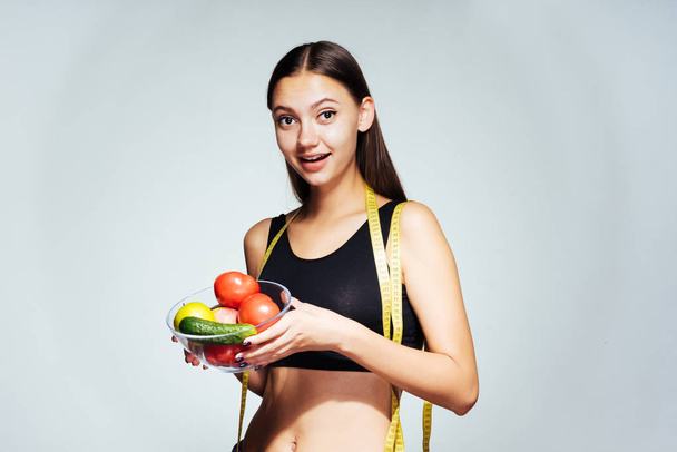 urheilullinen tyttö katsomassa hänen ruumiinsa, pitämällä lautasen hyödyllisiä vihanneksia ja hedelmiä
 - Valokuva, kuva