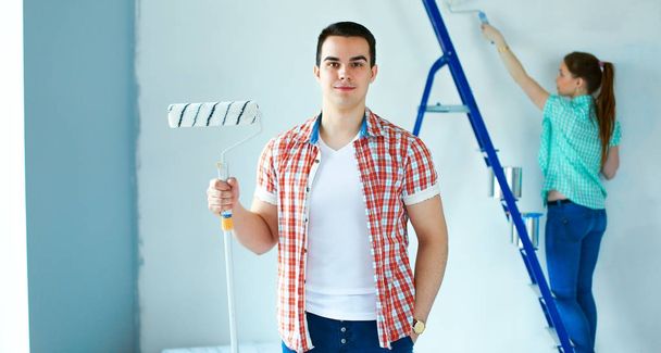 Portrait of happy smiling young couple painting interior wall new house - Фото, изображение