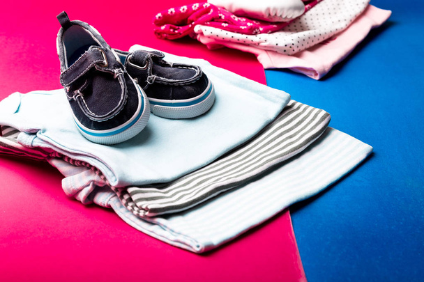 Folded blue and pink bodysuit with boat shoes on it on minimalistic pink and blue background. diaper for newborn boy and girl. Stack of infant clothing. Child outfit - Φωτογραφία, εικόνα