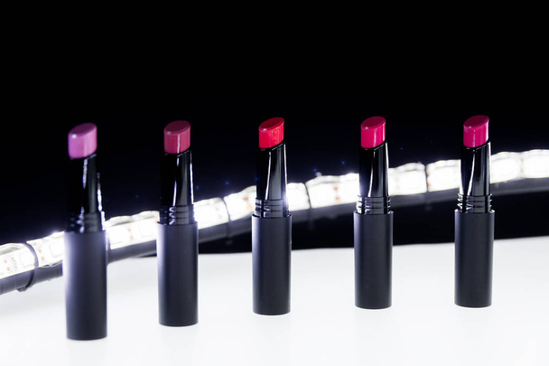 Instellen van matte Lipstick in rood en natuurlijke kleuren op witte en zwarte achtergrond. Mode kleurrijke lippenstiften. Professionele make-up en schoonheid. Knipperende bokeh achtergrond. - Foto, afbeelding