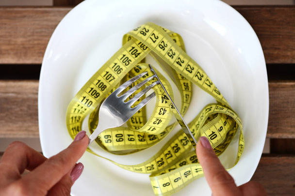 Concepto de dieta con la mujer preparada para comer una cinta métrica de plato blanco con cuchillo y tenedor, perder peso para ponerse en forma
 - Foto, Imagen