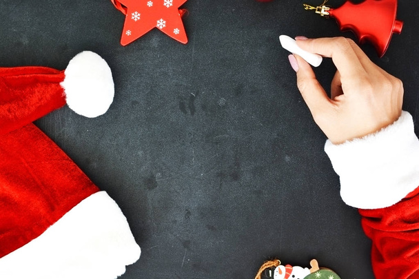 Fond de Noël avec les mains de la femme habillée en costume de Santas écrit sur tableau noir vide avec des décorations saisonnières
 - Photo, image