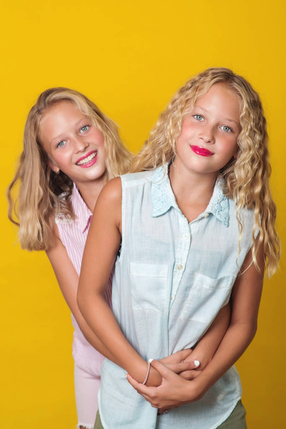 Близнецы девочки-подростки веселятся вместе, изолированные на желтом фоне
. - Фото, изображение