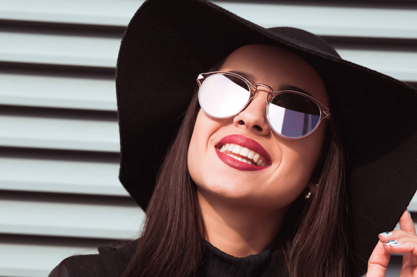 Jeune modèle souriant en lunettes de soleil et chapeau posant dans la rue
.  - Photo, image
