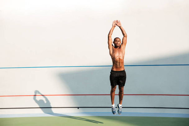 Full length portrait of a half naked african fitness man jumping - 写真・画像